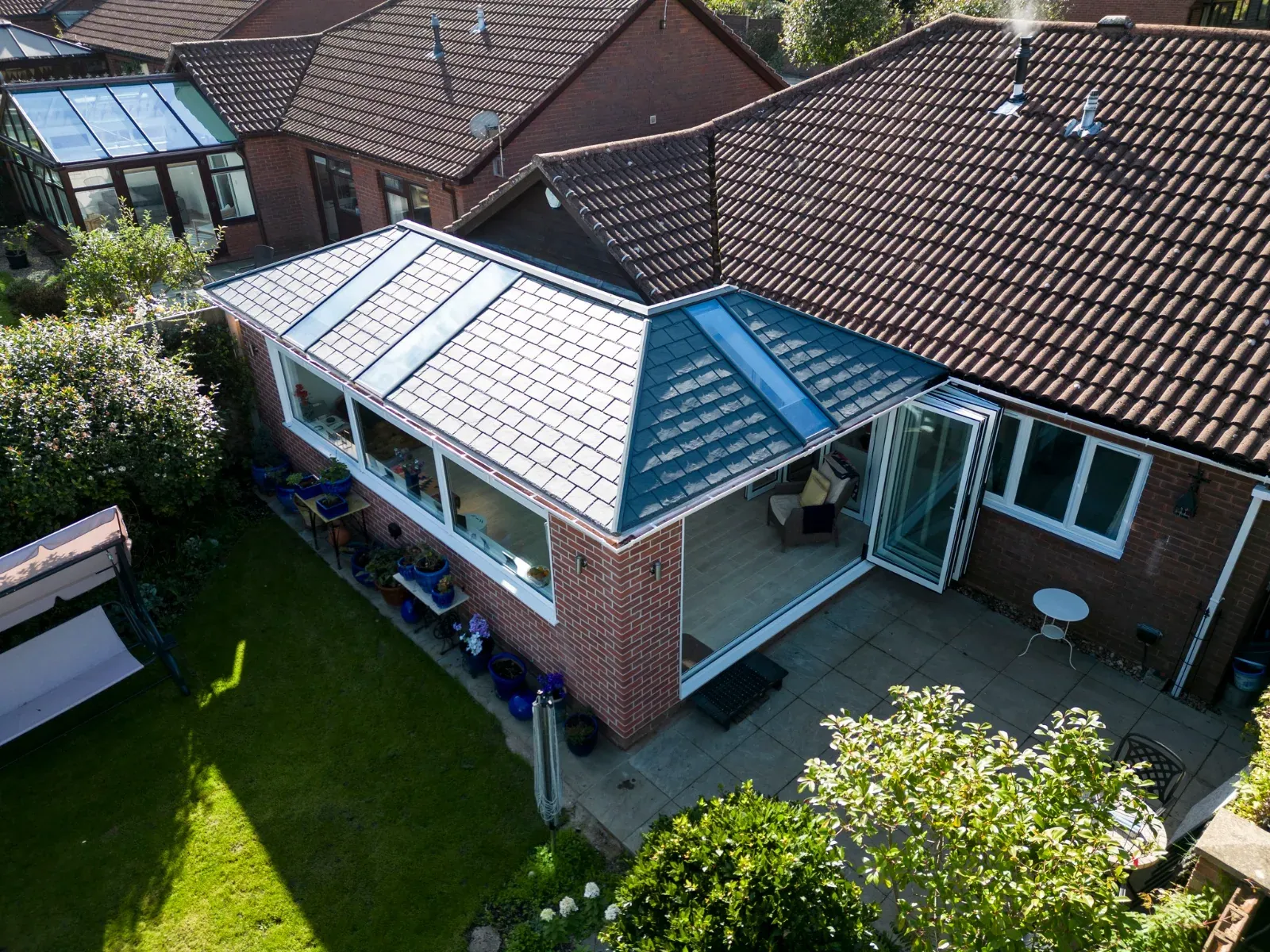 Aerial view of a modern tiled warm-roof extension with a glazed lantern, bifold doors open onto a bright interior and paved patio